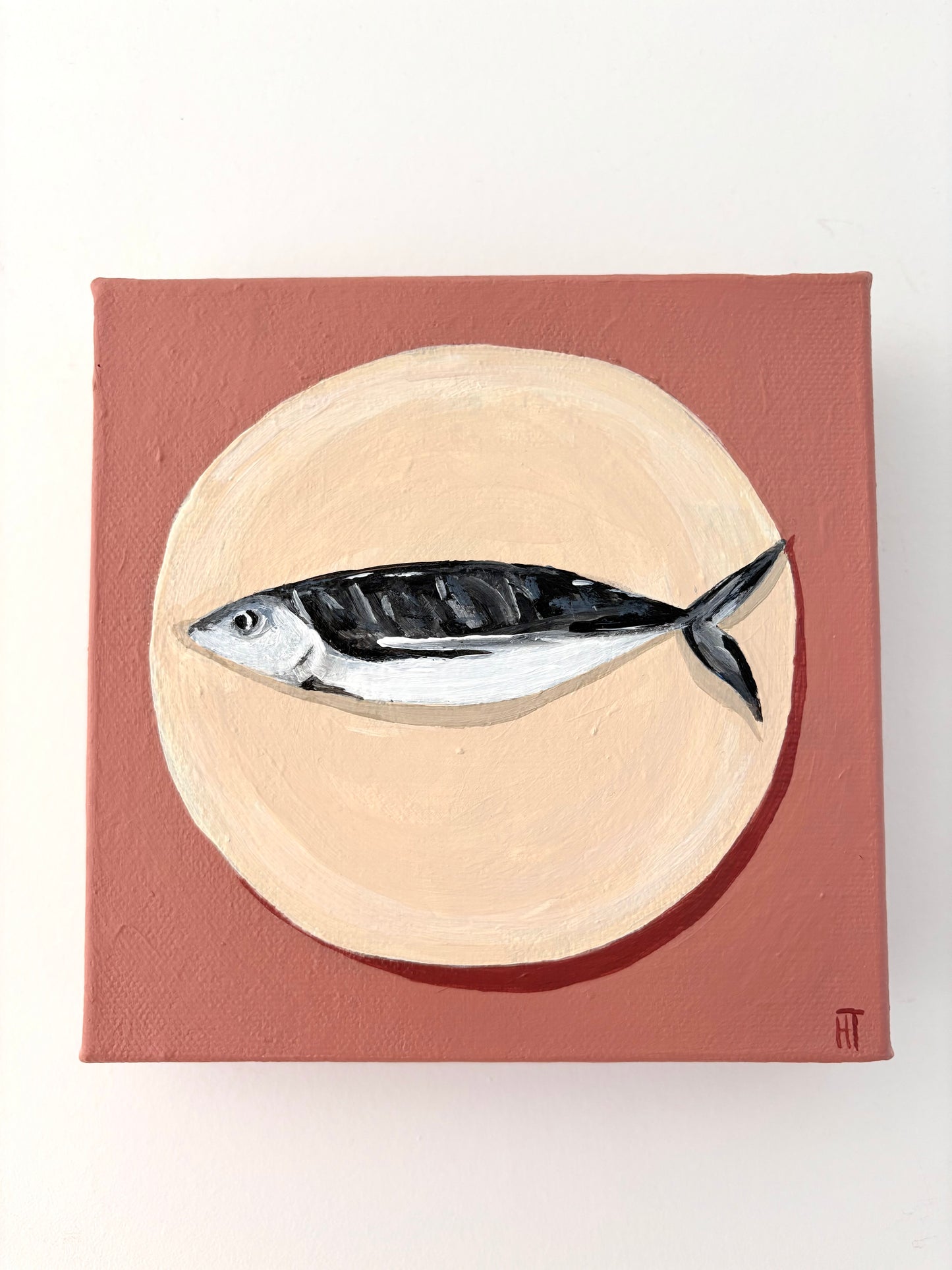 Painting of a fish on a beige circle plate with a dusty pink background.