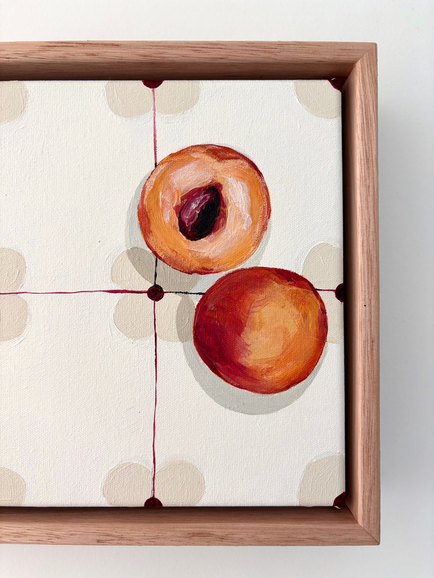 Halved peach on a patterned table cloth in an oak frame.