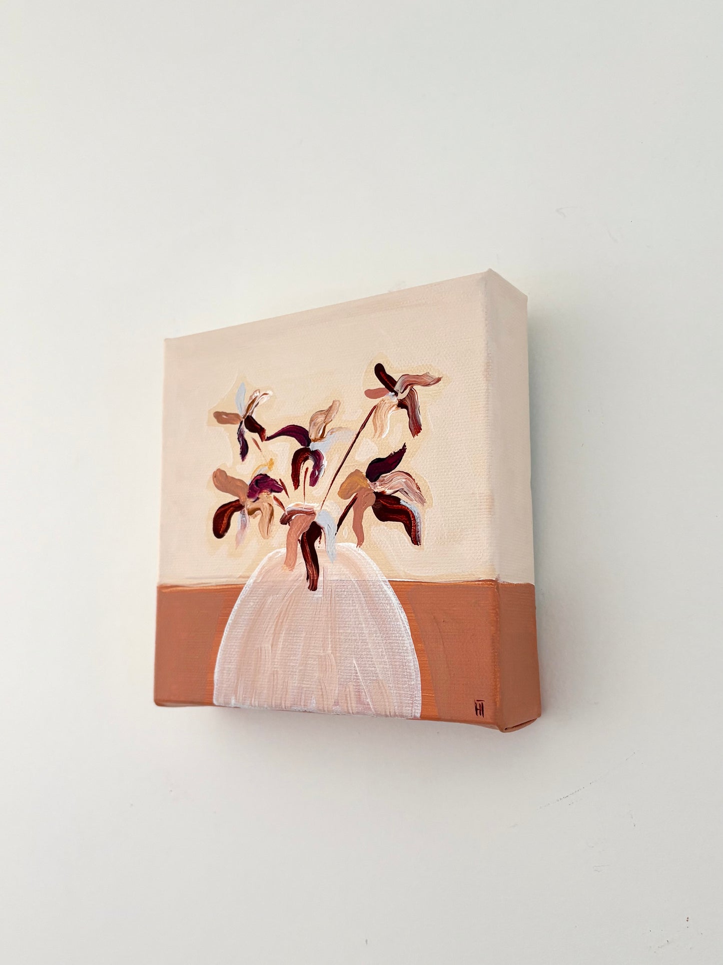 Brown and pink abstract flower arrangement in a white vase with a split burnt orange and cream background.