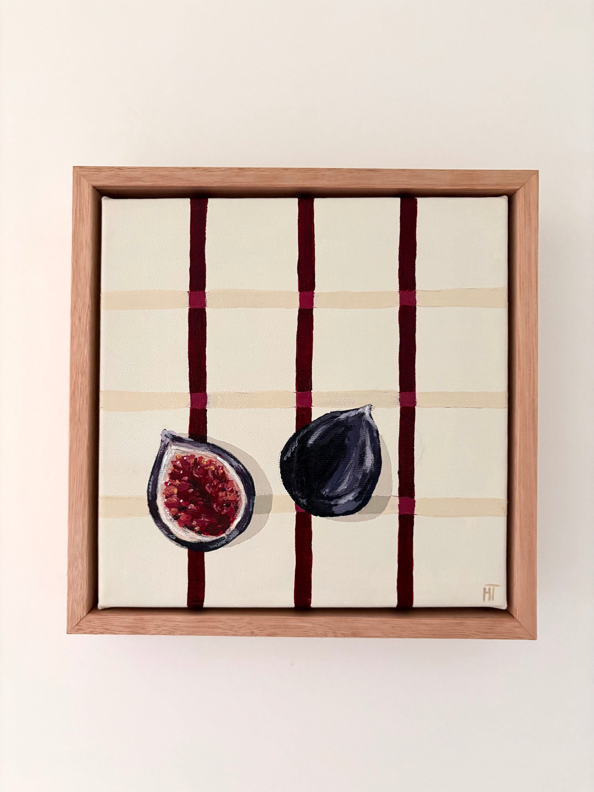 Painting of a halved dark fig on a cream checkered background with burgundy lines.Framed in oak.