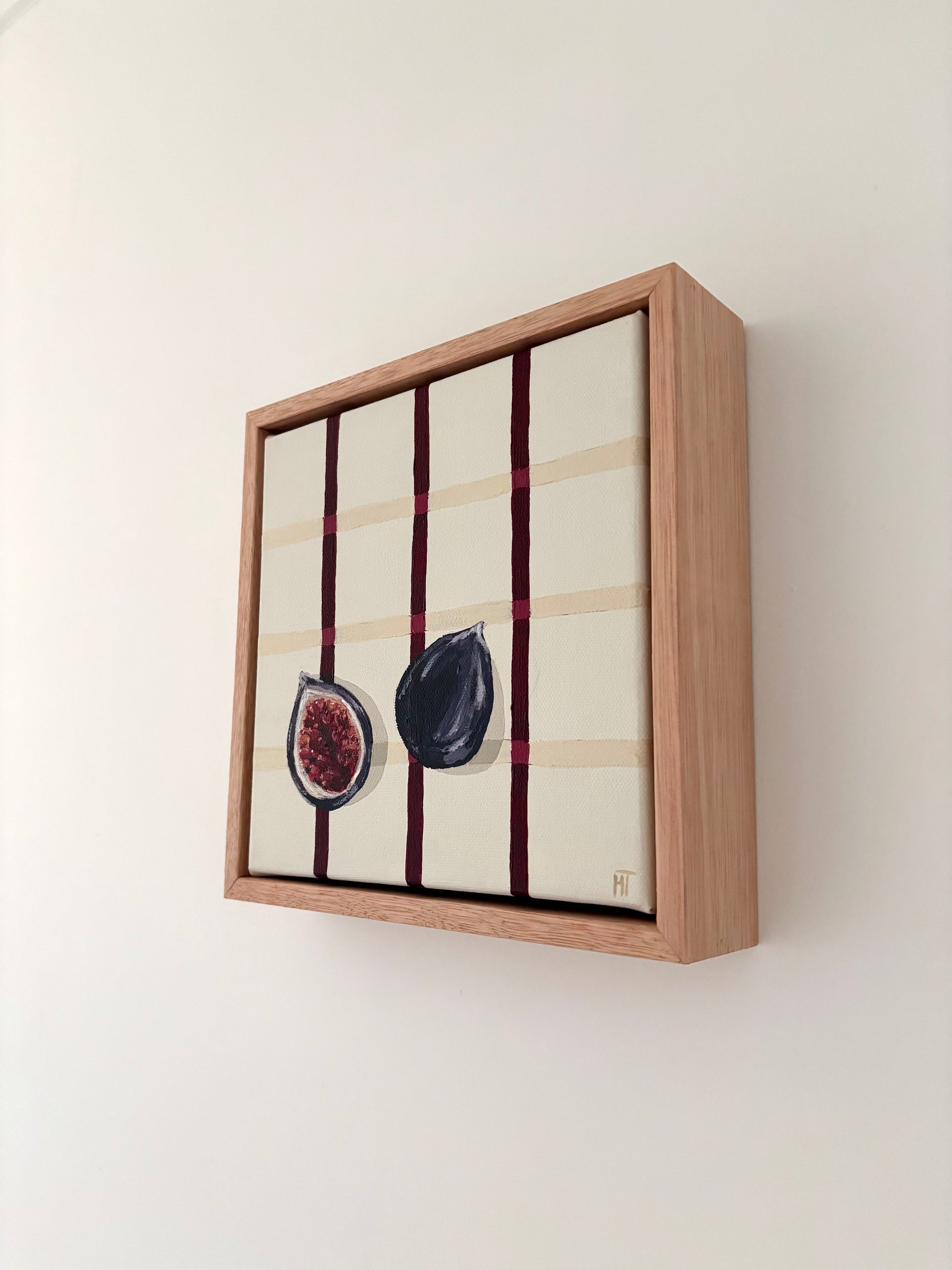 Painting of a halved dark fig on a cream checkered background with burgundy lines.Framed in oak.