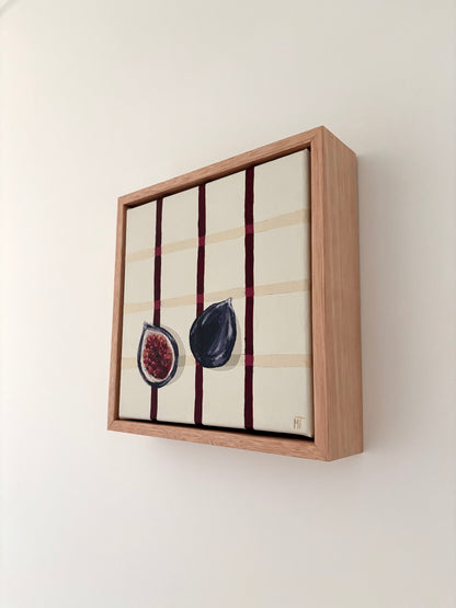 Painting of a halved dark fig on a cream checkered background with burgundy lines.Framed in oak.