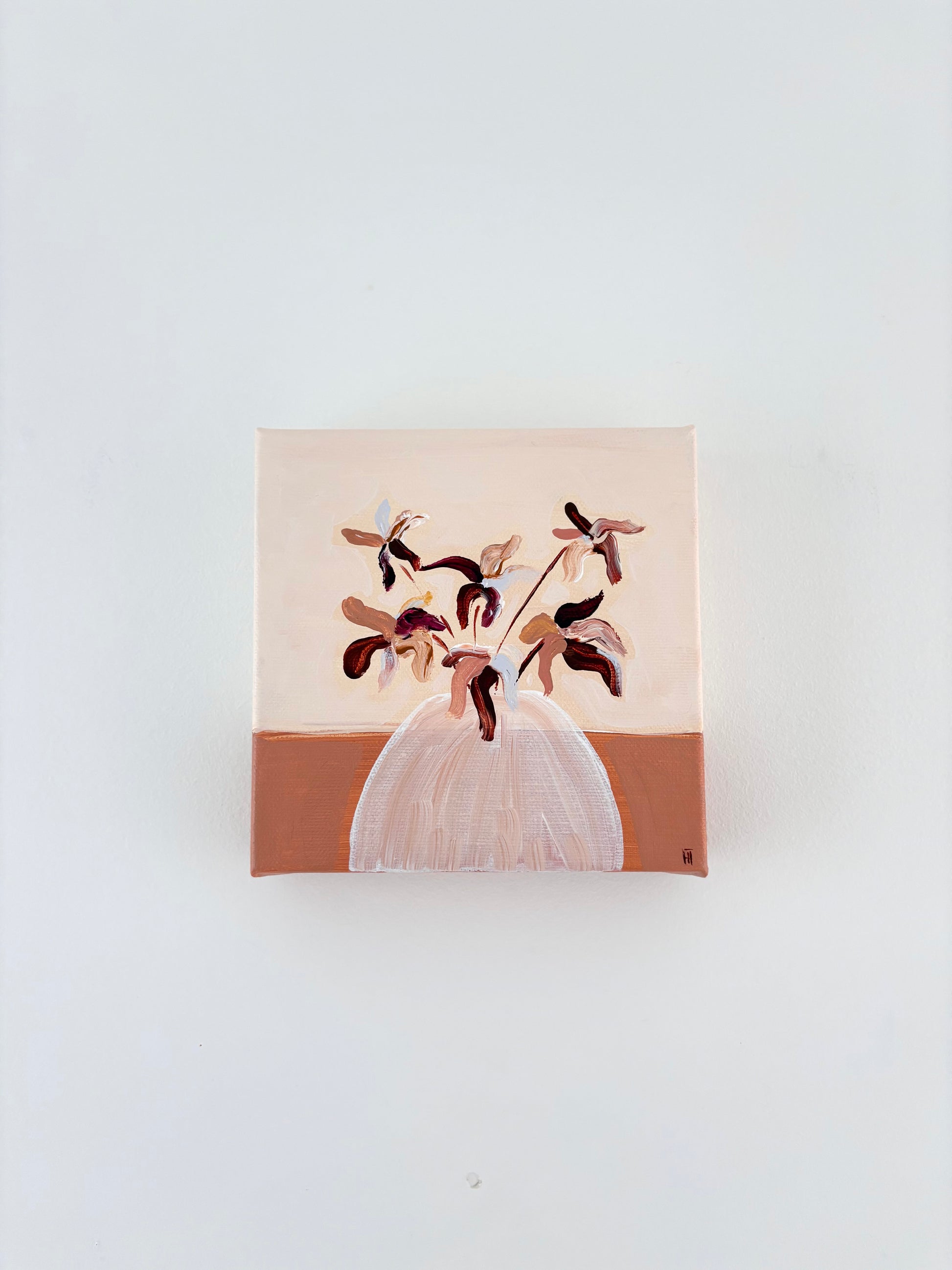 Brown and pink abstract flower arrangement in a white vase with a split burnt orange and cream background.