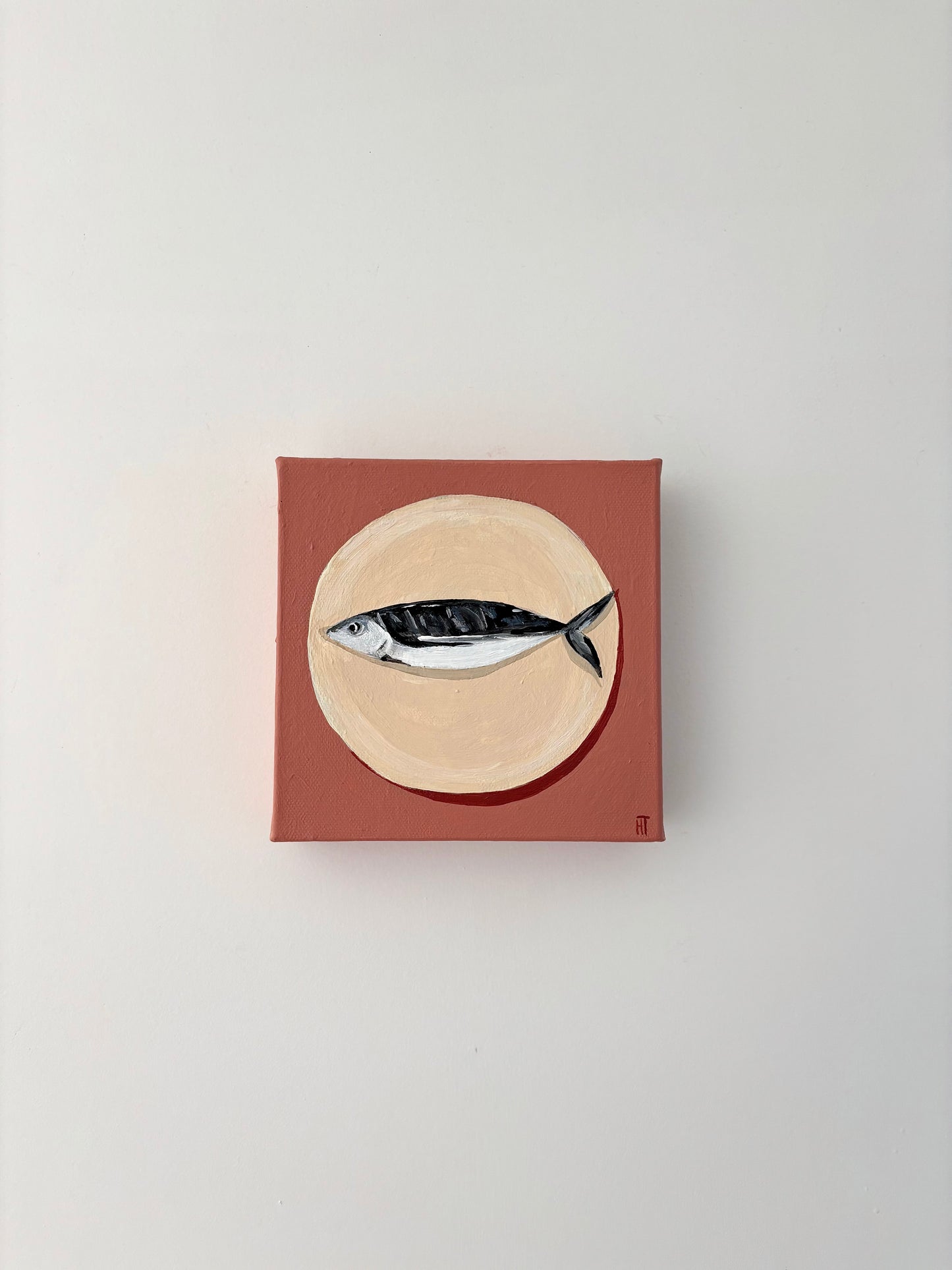 Painting of a fish on a beige circle plate with a dusty pink background.