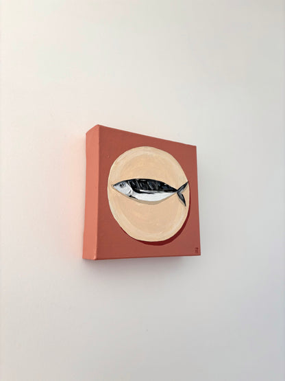 Painting of a fish on a beige circle plate with a dusty pink background.