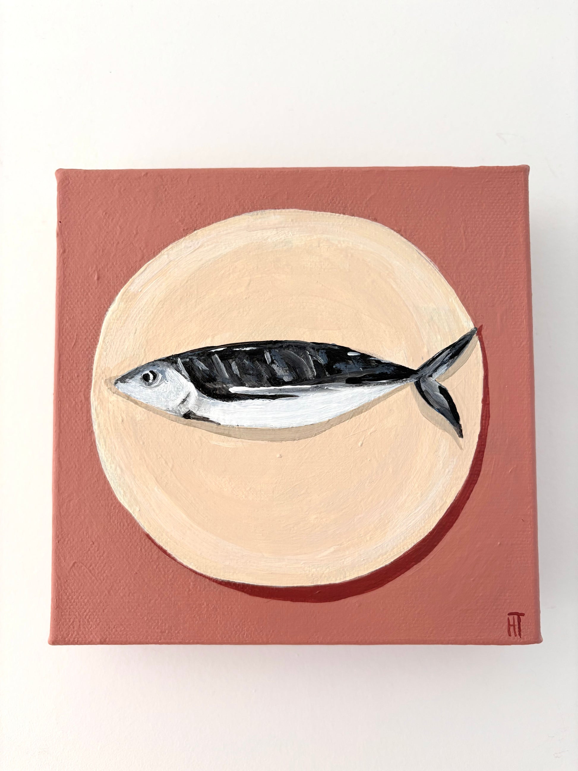 Painting of a fish on a beige circle plate with a dusty pink background.